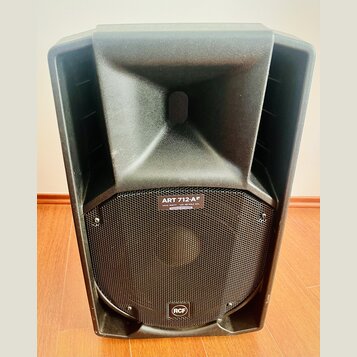 Černý aktivní reproduktor s plastovým krytem a kovovou mřížkou. Na horní části mřížky je nápis ART 712-AF a pod ním text 1400 WATT — 128 dB MAX SPL S…