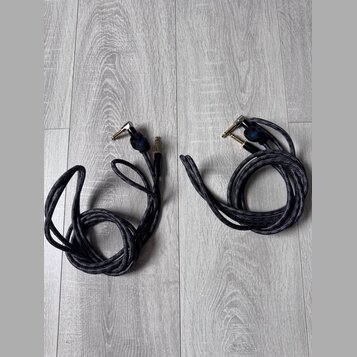 Dvě černé pletené audio kabelové spoje s úhlovým a rovným konektorem. Na obou kabelech je u konektorů viditelné modré logo s nápisem "Savage". Kabely…