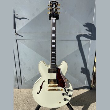 Kytara typu semi-akustika v krémové barvě s hnědočerveným pickguardem a zlatými komponenty. Na hlavě je bílý nápis Epiphone. Hриф má vložky z perlece…