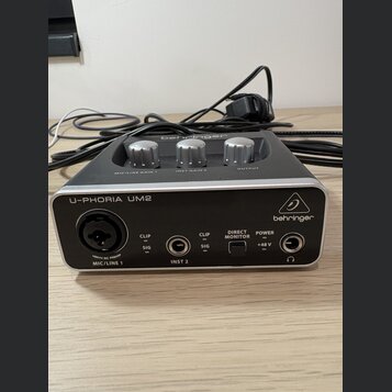 Kompaktní zvuková karta v šedé barvě s kovovým povrchem. Na přední straně je nápis U-PHORIA UM2 a logo behringer. Jsou zde vidět vstupy MIC/LINE 1 (X…