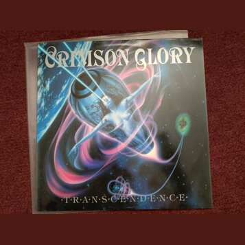 Fotografie zobrazuje obal vinylové desky s nápisem CRIMSON GLORY v horní části a TRANSCENDENCE v dolní části. Na obalu je surrealistický obraz ženské…