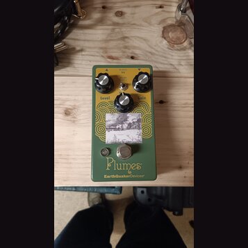 Zelený kytarový efekt s nápisy Plumes a EarthQuakerDevices®. Na horní straně jsou tři černé kontrolní knoflíky s popisky Level, Tone a Gain a přepína…