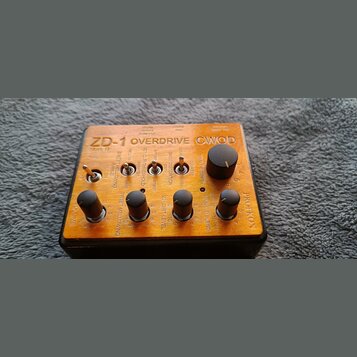 Kytarový efekt v oranžovém provedení s nápisem ZD-1 OVERDRIVE CWOD Mark II. Na horní straně jsou čtyři ovládací knoflíky, tři přepínače a nápis PROFK…