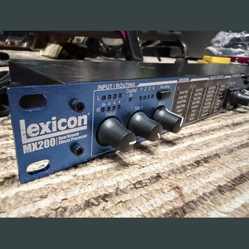 Modrý rackový efektový procesor s nápisem Lexicon MX200 Dual Reverb Effects Processor. Na předním panelu jsou tři černé otočné ovladače a sekce INPUT…