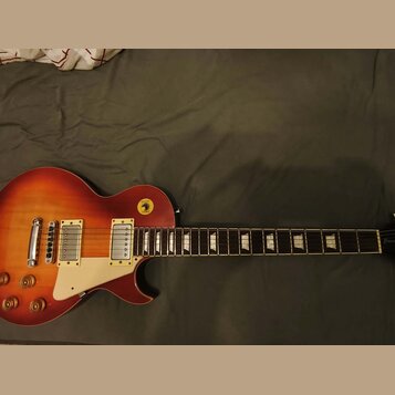 Elektrická kytara s tvarem singlecut a povrchovou úpravou v červeně-žlutém gradientu (sunburst). Má dva humbuckery, bílý pickguard a čtyři ovládací k…