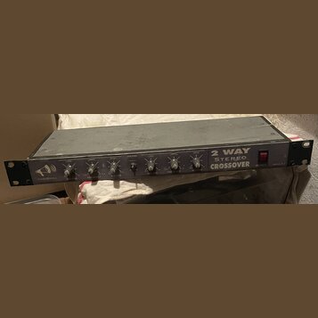 Černý rackový přístroj s nápisem 2 WAY STEREO CROSSOVER a logem AUDIOMAX. Na předním panelu se nachází šest otočných ovířkovaných potenciometrů s pop…