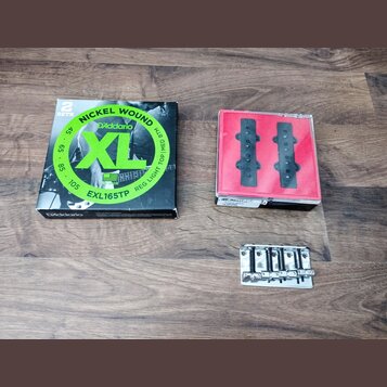 Fotografie zobrazuje tři předměty na hnědém dřevěném povrchu. Vlevo je černá krabička s nápisy NICKEL WOUND, D'Addario, XL a EXL165TP. Uprostřed je č…
