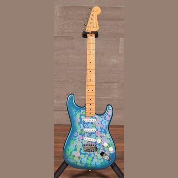 Modrá elektrická kytara s výrazným barevným vzorem květin na těle. Na hlavě hředu je viditelné logo Fender. Nástroj má světlou dřevěnou hmatnici a tř…