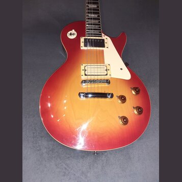 Elektrická kytara s tvarem singlecut a povrchovou úpravou v červeno-žlutém přechodu (sunburst). Nástroj má dva humbuckery, bílý plechtrum a čtyři zla…