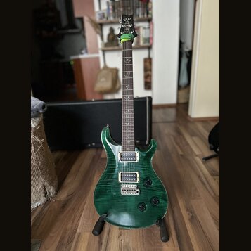 Zelená elektrická kytara s výraznou strukturou dřeva na těle a hnedým hmatníkem. Na hlavě je viditelné logo PRS. Kytara má dva humbuckery, fixační mo…