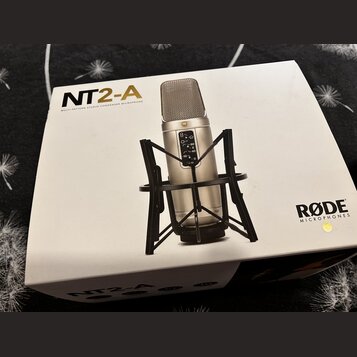 Bílá krabice s nápisem NT2-A MULTI-PATTERN STUDIO CONDENSER MICROPHONE a logem RØDE MICROPHONES. Na krabici je zobrazen stříbrný kondenzátorový mikro…