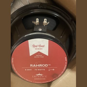 Fotografie zachicuje zadní stranu reproduktoru s červenobílou nálepkou. Na nálepce jsou nápisy RAMROD TM, 75 WATTS, 8 OHM, Red Coat SERIES, PREMIUM B…