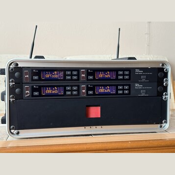 Hliníkový přepravní kufr obsahuje dva černé bezdrátové přijímače značky Letone, model free solo Twin DR 590 MHz. Každý přijímač má digitální displej…