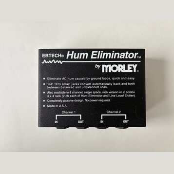 Černý box s nápisem EBTECH® Hum Eliminator™ by MORLEY®. Na povrchu je text popisující funkce zařízení a poznámka Made in U.S.A. V dolní části jsou dv…