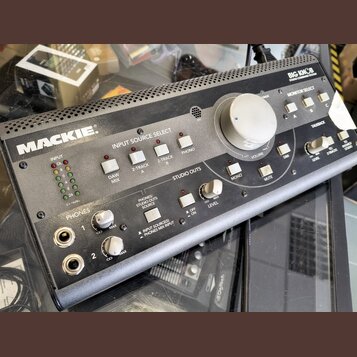 Šedý monitorovací kontrolér značky MACKIE s nápisem BIG KNOB STUDIO COMMAND SYSTEM. Zařízení obsahuje velký centrální knofík VOLUME, sekci INPUT SOUR…