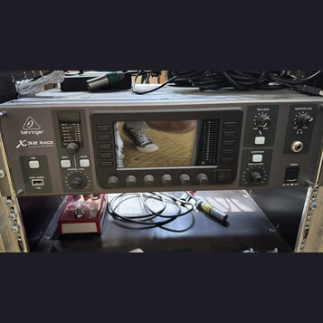 Šedý rackový digitální mixér s nápisem behringer X32 RACK POWERED BY MIDAS. Zařízení má centrální displej, několik ovládacích tlačítek a pět otočných…