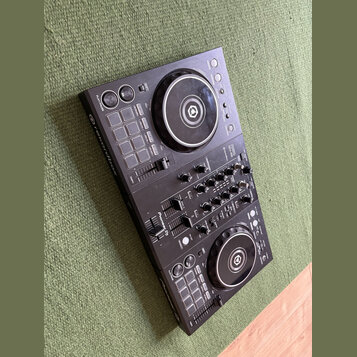 Černý DJ 컨트롤러 s dvěma jogovými koly a centrálním mixážním sekcí. Na přístroji jsou viditelné nápisy rekordbox, Pioneer DJ a model DDJ-400. Povrch je…