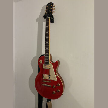 Červená elektrická kytara typu Les Paul s bílým pickguardem a dvěma humbuckery. Na hlavě je zlatý nápis „Les Paul“ a podpis „Jimmy Page“. Kytara má z…