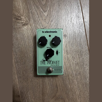 Světle zelený kytarový efekt s nápisem tc electronic a THE PROPHET DIGITAL DELAY. Na horní straně jsou dva černé otočné oválné knoflíky s popisky TIM…
