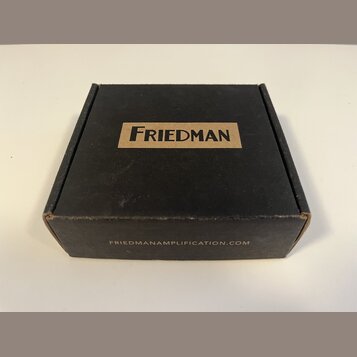 Černá papírová krabička s hnědým obdélníkovým polem, ve kterém je černý nápis FRIEDMAN. Na spodní hraně krabice je uveden web FRIEDMANAMPLIFICATION.C…