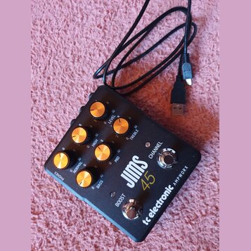 Černý kytarový předzesilovač s nápisy JIMS 45 a tc electronic AMPWORX. Zařízení má zlaté otočné knoflíky s popisky LEVEL, TREBLE, HIGH, MID, NORMAL a…