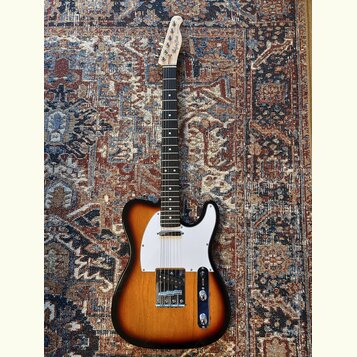 Elektrická kytara typu Telecaster s tělem v provedení sunburst a bílým pickguardem. Na hlavě hředu je viditelné logo "Fender". Kytara má tmavý hmatní…