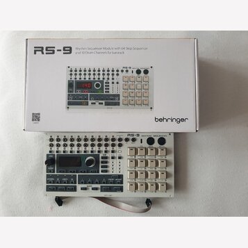 Na fotografii je bílý modul Rhythm Sequencer RS-9 od značky behringer, umístěný před svým původním kartónovým obalem. Modul má bílé provedení s černý…