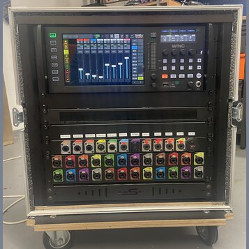 Digitální mixovací pult BEHRINGER WING umístěný v rackovém kufru s pěnovým vnitřkem. Pod mixem se nachází rozhraní s řadou barevných konektorů a nápi…