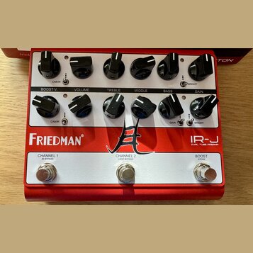 Červený kytarový předzesilovač s bílým horním panelem. Na červeném spodním panelu jsou nápisy Friedman, IR-J DUAL TUBE PREAMP a logo ve tvaru stylizo…