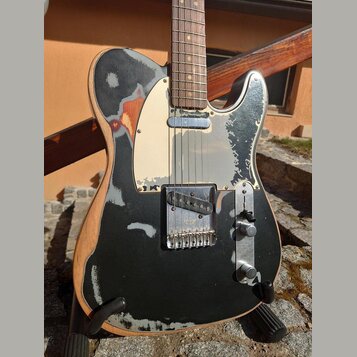 Elektrická kytara typu Telecaster s černým lakem, který je výrazně opotřebovaný a v mnoha místech odloupaný, čímž odhaluje světlé dřevo. Nástroj má k…