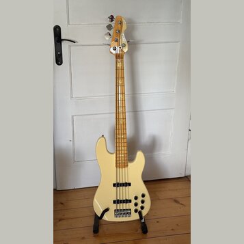 Světle béžová elektrická basová kytara s přírodním dřevěným hnedem krku a hmatníkem. Na hlavě je viditelné logo "Squier". Tělo nástroje má dva snímač…