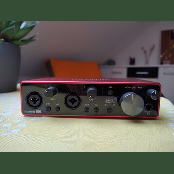 Červený audio rozhraní s černým předním panelem. Na panelu jsou dva vstupy, knoflíky GAIN a nápisy INST a AIR u obou kanálů, přepínač 48V, knoflík MO…