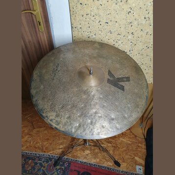 Zlatý činely s koncentrickými rýhami a viditelným opotřebením povrchu. Na ploše je černé logo ve tvaru velkého písmena K a nápis Custom Dry Ride. V d…