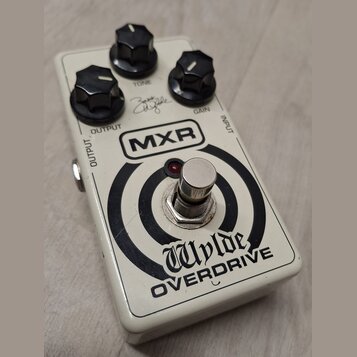 Bílý kytarový efekt MXR Wylde OVERDRIVE s černými oválnými knoflíky. Na horní straně jsou nápisy TONE, GAIN a OUTPUT, vedle nich je viditelný podpis.…
