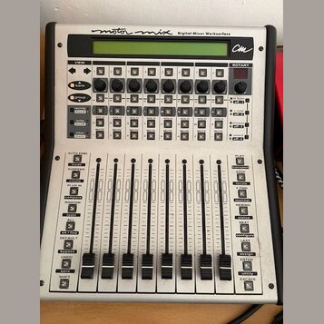 Stříbrný digitální mixovací kontroler s nápisem motor mix Digital Mixer Worksurface a logem cm. Zařízení obsahuje LCD displej, řadu otočných knoflíků…