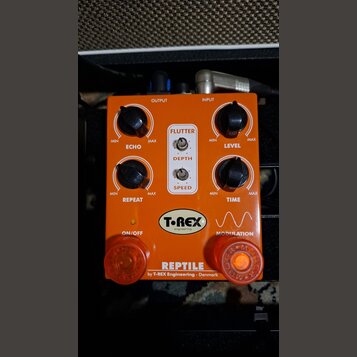 Oranžový kytarový efekt s nápisem REPTILE by T-REX Engineering - Denmark. Na horní straně jsou čtyři černé otočné ovladače s popisky ECHO, LEVEL, REP…