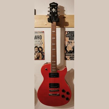 Červená elektrická kytara s tvarem připomínajícím Les Paul, umístěná na nástěnním držáku. Na hlavě je bílý nápis Washburn a logo ve tvaru stylizované…
