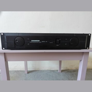 Černý rackový zesilovač s nápisem SAMSON STUDIO AMPLIFIER 85 WATT STEREO SERVO-170. Na předním panelu jsou dvě velké otočné potenciometry, vypínač PO…