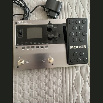 Stříbrný kytarový procesor s černým expresním pedálem, na kterém je bílý nápis MOER. Na horní části přístroje je text GE150 Amp modelling & Multi Eff…