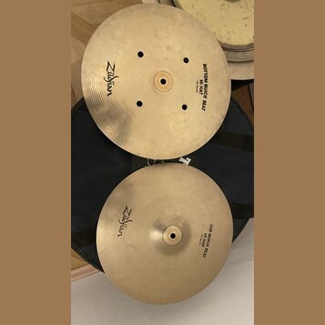 Dva mosazné činely typu hi-hat položené na černém obalu. Horní činel má nápisy Zildjian a BOTTOM QUICK BEAT HI HAT 14"35cm. Dolní činel nese nápisy Z…