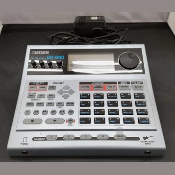 Stříbrný digitální doprovodný modul s nápisem BOSS DrRhythm DR-880. Zařízení má horní panel s ovládacími knoflíky, displejem a pravým volitkem, spodn…