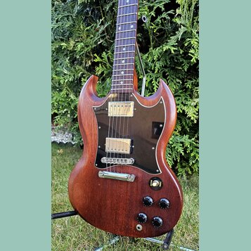 Elektrická kytara s hnědým dřevěným tělem a tmavým hnedým plechtrátem. Nástroj má dva humbuckery s kovovými kryty, čtyři otočné knoflíky a přepínač s…