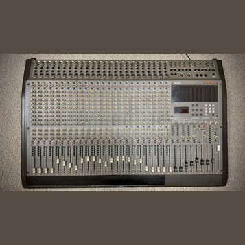 Široký míchací pult s šedým povrchem a černým rámem. Na pravé straně je červené logo TASCAM a vedle něj vertikální nápis M-2524. Přístroj obsahuje ve…