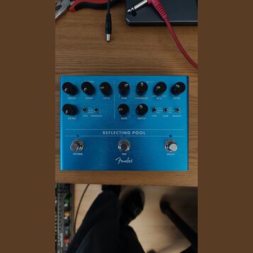 Modrý kytarový efekt s nápisem REFLECTING POOL a logem Fender. Zařízení má tři spínací tlačítka označená jako REVERB, TAP a DELAY. Na pravé straně se…