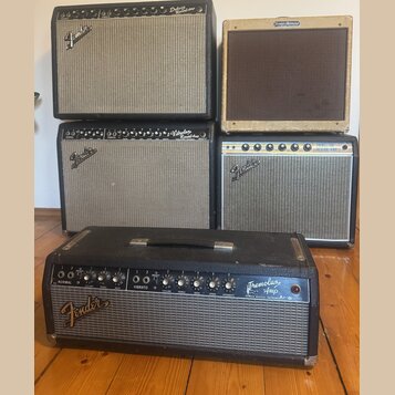 Fotografie zobrazuje pět kytarových komb značky Fender. V horní řadě je černý zesilovač s nápisem Deluxe Reverb Amp a béžový zesilovač s nápisem Fend…