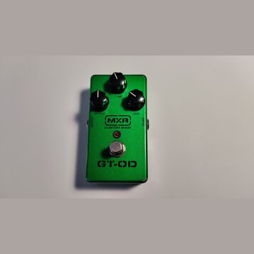 Zelený kytarový efekt s kovovým šasi. Na horní straně jsou tři černé ovládací knoflíky s popisky OUTPUT, TONE a GAIN. Uprostřed je logo MXR a nápis C…