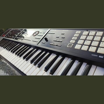 Černý digitální klavír s bílými a černými klávesami. Na ovládacím panelu jsou viditelné nápisy ARPEGGIO/RHYTHM, SEQUENCER a SAMPLER, množství bílých…
