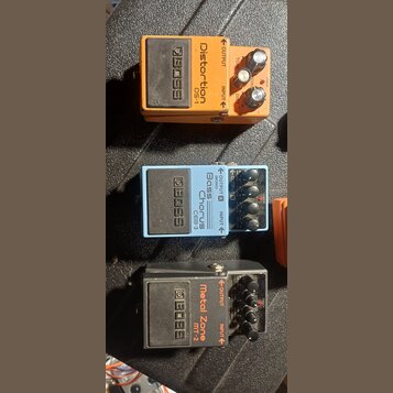 Tři kytarové efekty značky BOSS v kovovém provedení. Horní oranžový pedál má nápis Distortion PS-1, prostřední světle modrý Chorus CEB-3 Bass a spodn…