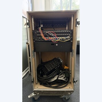 Otevřený transportní rack na kolečkách, v němž jsou namontovány dvě černé zařízení. Horní jednotka nese nápis Soundcraft MINI STAGEBOX 32 a má zapoje…
