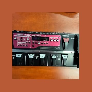 Černý loop pedal s výrazným růžovým ovládacím panelem. Na panelu je bílý nápis BOSS RC-300 LOOP STATION a digitální displej. V dolní části jsou pět č…